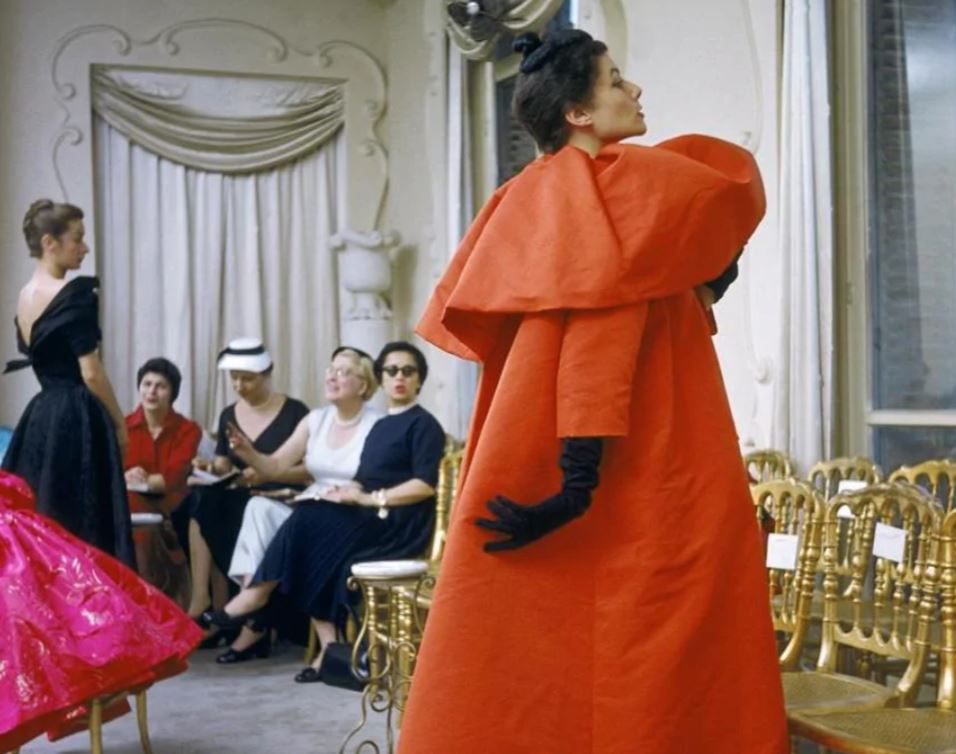 Modella con soprabito rosso, guanti e cappello neri, sfila nell'atelier Balenciaga, 1954