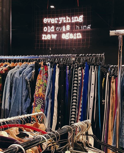 Il motto di East Market scritto con le luci che illuminano uno stand di abbigliamento vintage in una precedente edizione