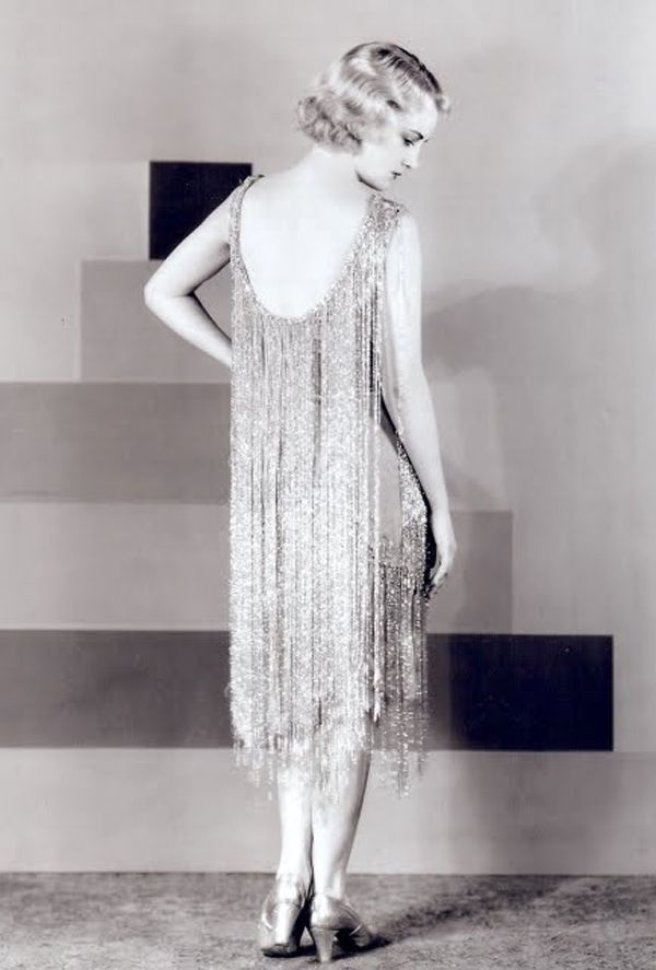 Giovane donna bionda indossa un abito scollato sulla schiena con lunghe frange luccicanti, anni '20