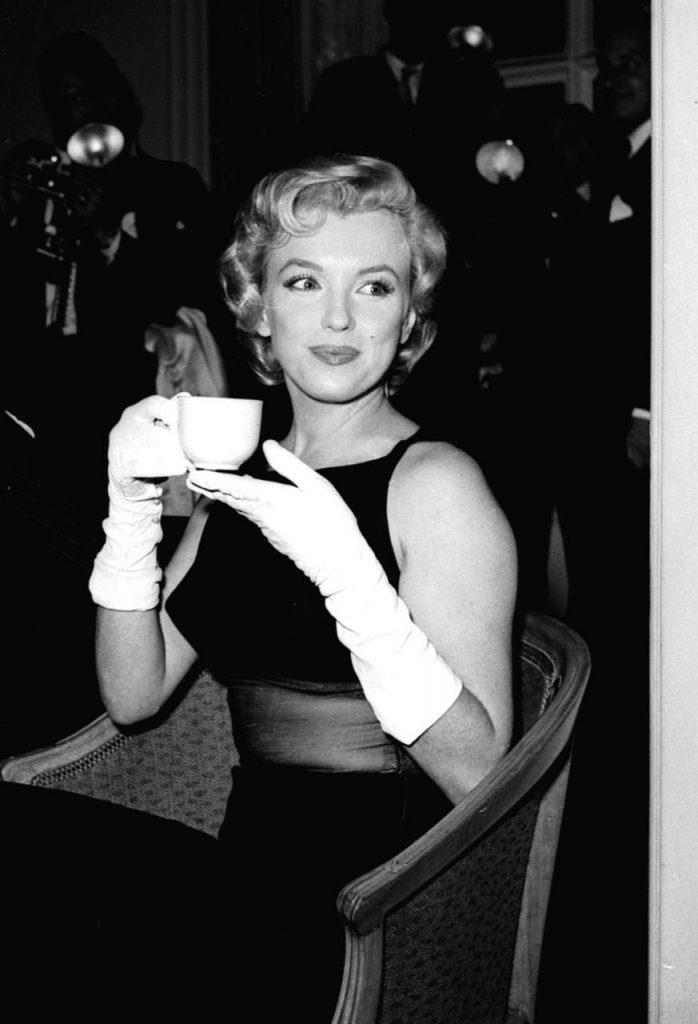 Marilyn Monroe seduta con una tazzina in mano indossa un tubino nero con inserto trasparente e guanti bianchi