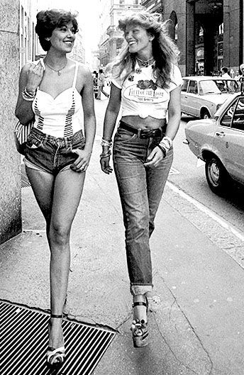 Due ragazze degli anni Settanta: una indossa hot pants e canotta bianca, l'altra jeans classici e t-shirt bianca annodata.
